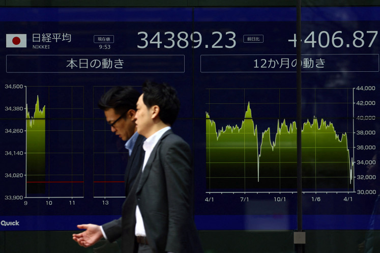 Passersby walk past an electronic screen displaying Japan's Nikkei share average in Tokyo on April 15, 2025.