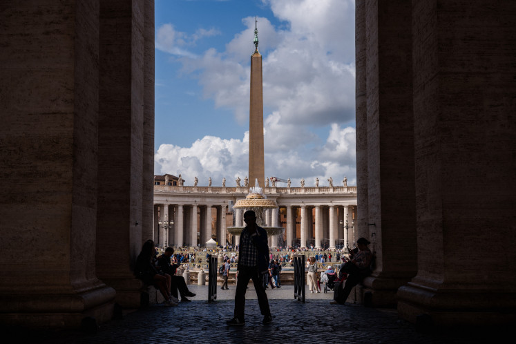A visitor walks under the colonnade, with a view of the obelisk in the background at the Vatican on May 5, 2025.