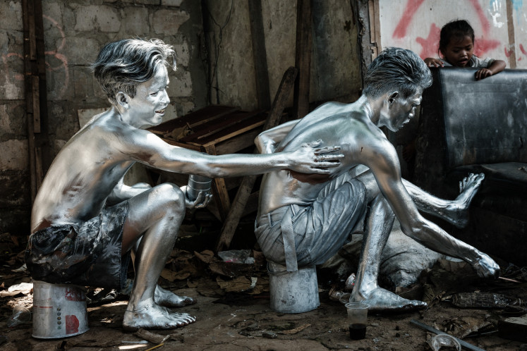 This photo taken on April 7, 2025 shows street performers Keris Munandar (right) and his neighbor Riyan Ahmad Fazriyansah painting their bodies silver in Jakarta.