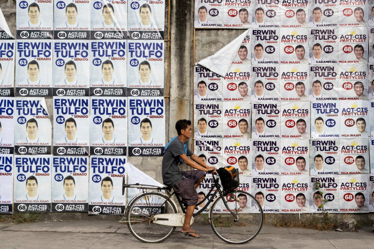 A man bikes past a wall of campaign posters for senatorial candidate Erwin Tulfo on the first day of the campaign period for the May 12 midterm elections, in Manila, the Philippines, on Feb. 11, 2025.