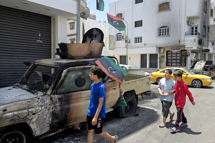 A Libyan flag flutters on a destroyed car as children walk past following overnight clashes in the southern district of Abu Salim in the capital Tripoli on May 13, 2025. Overnight clashes in Libya's capital killed at least six people, an emergency medical service said on May 13, with local media reporting that an armed group leader was among the dead.