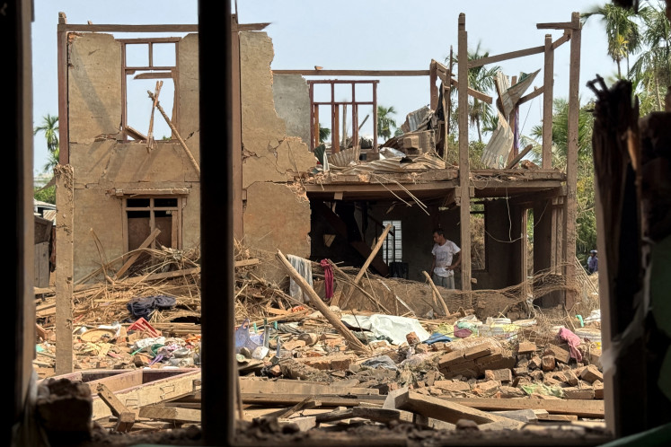 People assess damaged buildings following Myanmar military airstrikes in Kyauktaw town in Myanmar's western Rakhine State on May 15, 2025. 