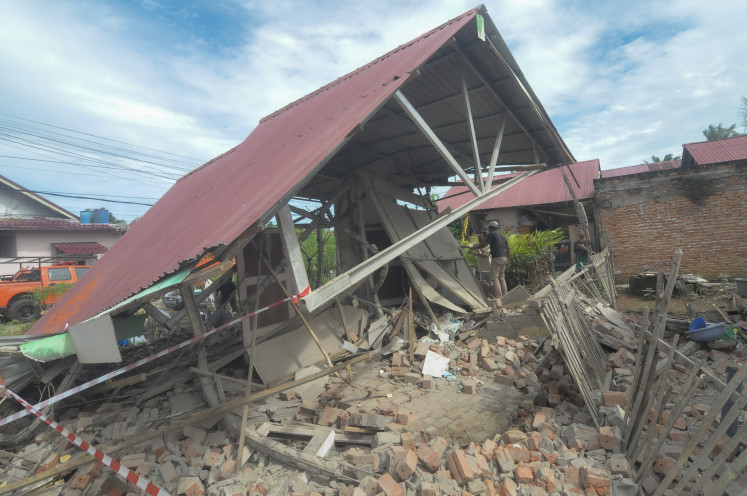 A man stands atop a pile of broken masonry under the precariously suspended roof of a collapsed house on May 23, 2025, following a 6.3-magnitude earthquake in Bengkulu, the capital of Bengkulu province on the southwest coast of Sumatra.