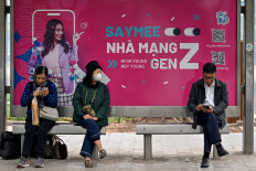 People use their phones at a bus stop, in front of an advertising billboard referencing “Gen Z“, in Hanoi on December 25, 2024.