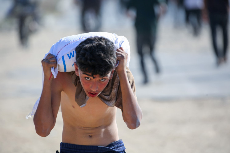 A displaced Palestinian youth carries a bag of food aid on his shoulders after people stormed a World Food Programme warehouse in Deir el-Balah in the central Gaza Strip on May 28, 2025. The United Nations on May 28 condemned a US-backed aid system in Gaza following a chaotic food distribution where 47 people were injured, after Israel allowed supplies in at a trickle last week, easing a full blockade imposed on the besieged Palestinian territory for over two months.