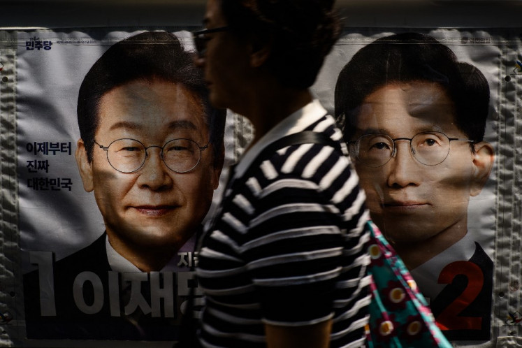 A woman walks past a banner showing (from left to right) Lee Jae-myung, the presidential candidate for the Democratic Party, and Kim Moon-soo, the presidential candidate for the conservative People Power Party, displayed outside a polling station during the second day of early voting for the presidential elections in Seoul on May 30, 2025.