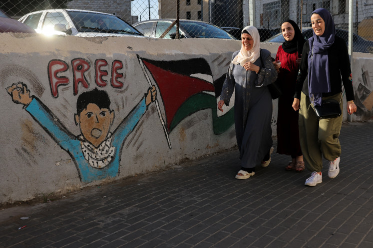 Palestinian women walk past a mural in Ramallah, in the occupied West Bank, on May 31, 2025.
