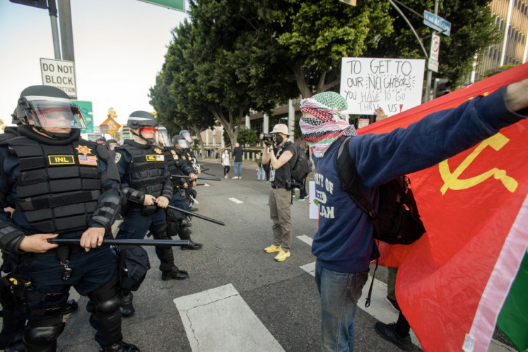 A demonstrator in a multicoloured keffiyeh holds up the Soviet Union Flag as protesters clash with law enforcement in the streets surrounding the federal building during a protest following federal immigration operations in Los Angeles, California, on June 8, 2025. 