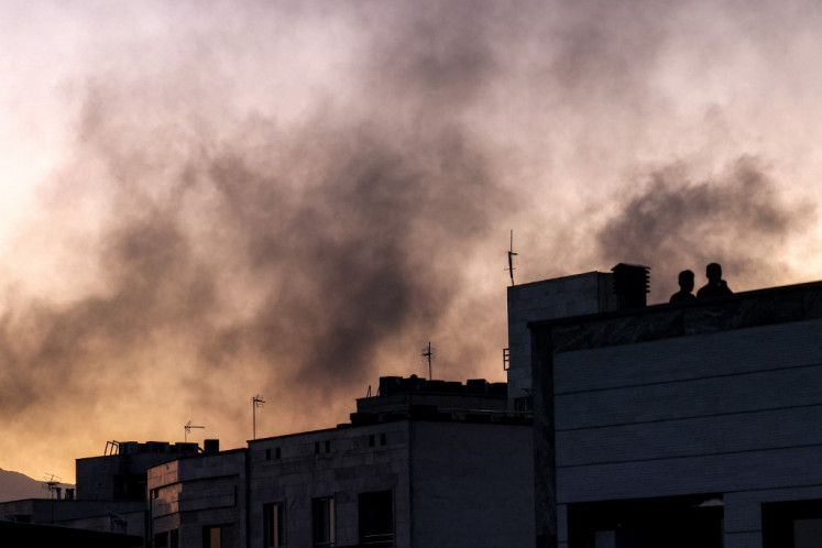 People stand on a rooftop amidst billowing smoke following an overnight Israeli strike in Tehran on June 17, 2025.