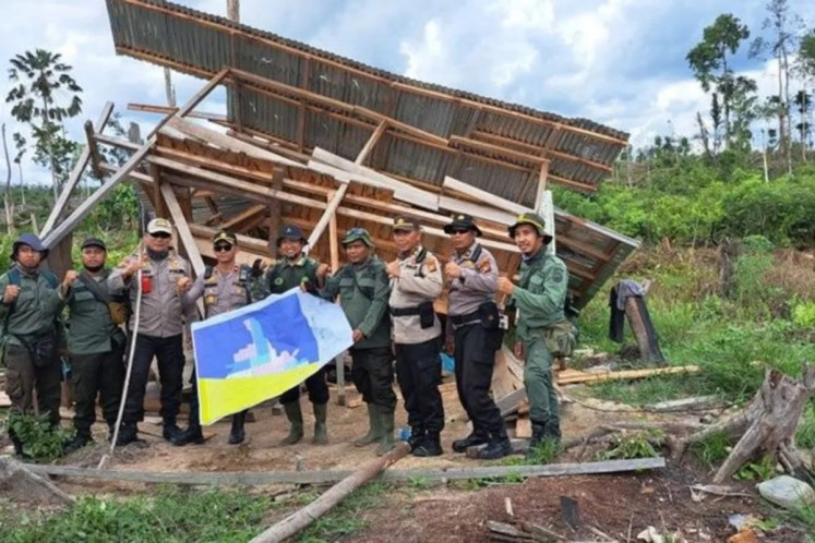 Forest rangers and policemen pose in front of a demolished illegal structure inside the Tesso Nilo National Park in Pelalawan regency, Riau, on June 10, 2025. The personnel are part of the Garuda Task Force deployed to rehabilitate forest areas.  