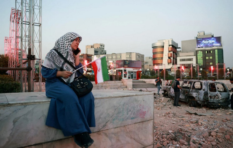 An Iranian woman sits close to a destroyed vehicle as she watches and listens to a traditional band as it performs to show solidarity with the Iranian people at Hafteh-tir Square, in Tehran, Iran on June 23, 2025.