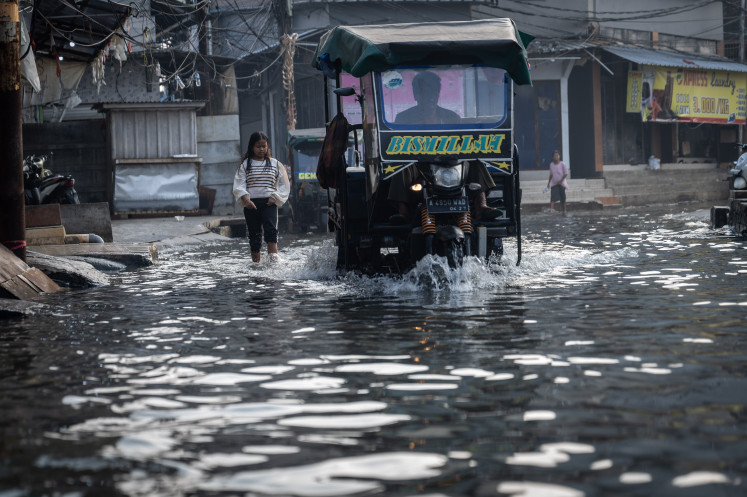 A girl stands in the wake of a ‘bajaj’ on June 25, 2025, as its driver plows through a flooded street in Muara Angke, North Jakarta. The Jakarta Disaster Mitigation Agency (BPBD) has advised northern coastal communities in the city that high tide flooding due to the super new moon on Wednesday could last until June 29.