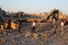 Palestinians walk past the rubble and destroyed vehicles in the Al-Bureij camp in the central Gaza Strip after a house was targeted by an Israeli strike on June 27, 2025, amid the ongoing conflict between Israel and the Palestinian Hamas militant group.