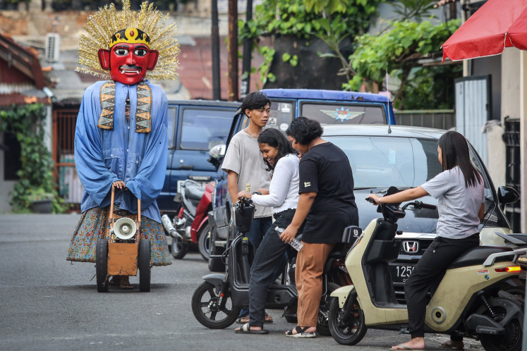 A street performer in an ‘ondel-ondel’ costume pushes a makeshift cart fitted with a megaphone on June 2, 2025, as youths mingle in a roadside parking area on Jl. Matraman Raya in East Jakarta. Governor Pramono Anung has proposed banning the use of the giant effigies in street performances in a new regulation to preserve ‘ondel-ondel’ as a symbol of Betawi heritage.
