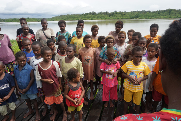Life at the river’s edge: The children of Mbu Agani village in Unir Sirau district in South Papua’s Asmat stand barefoot on a rain-slicked wooden platform by the riverbank, attentively listening to a village elder. JP/Dio Suhenda