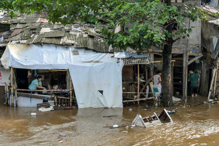 A woman (left) attempts to drain water from inside her home as floods hit her neighbourhood following heavy rainfall in Jakarta on July 7, 2025. 
