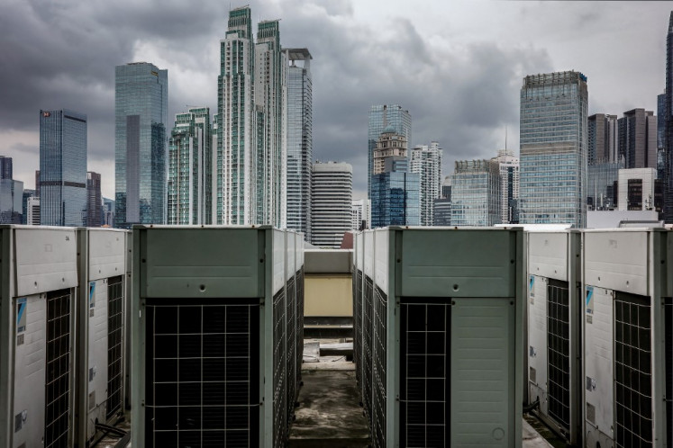 This picture taken on January 22, 2025 shows a row of outdoor AC units (foreground) on top of a building with a backdrop of Jakarta's cityscape. 