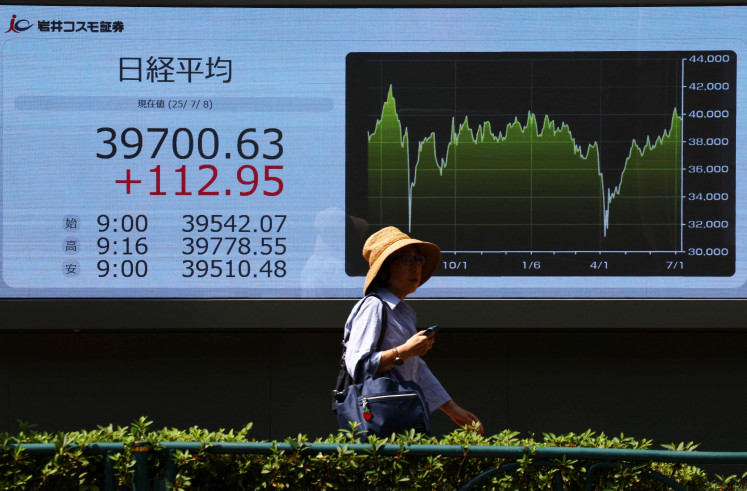 A woman walks past a screen displaying Japan's Nikkei share average outside a brokerage in Tokyo on July 8, 2025.