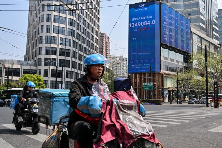 Motorists ride past a screen showing the gross domestic product (GDP) in the Jing'an district of Shanghai, China, on April 9, 2025.