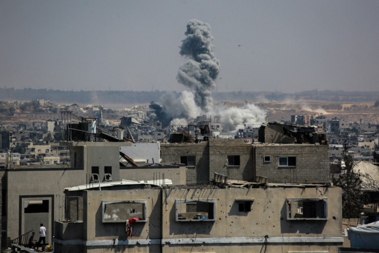 Two Palestinians stand on the roof of a building as smoke billows following Israeli strikes on Jabalia, in the northern Gaza Strip on July 13, 2025. Delegations from Israel and the Palestinian militant Hamas group have now spent a week trying to agree on a temporary truce to halt 21 months of devastating fighting in the Gaza Strip.