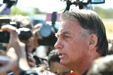 Brazil's former president Jair Bolsonaro speaks to members of the media after being fitted with an electronic monitoring device in Brasilia on July 18, 2025. Brazi's former president Jair Bolsonaro must wear an electronic monitoring device as he awaits a verdict in his trial on charges of plotting a coup, a Supreme Court judge ruled Friday.