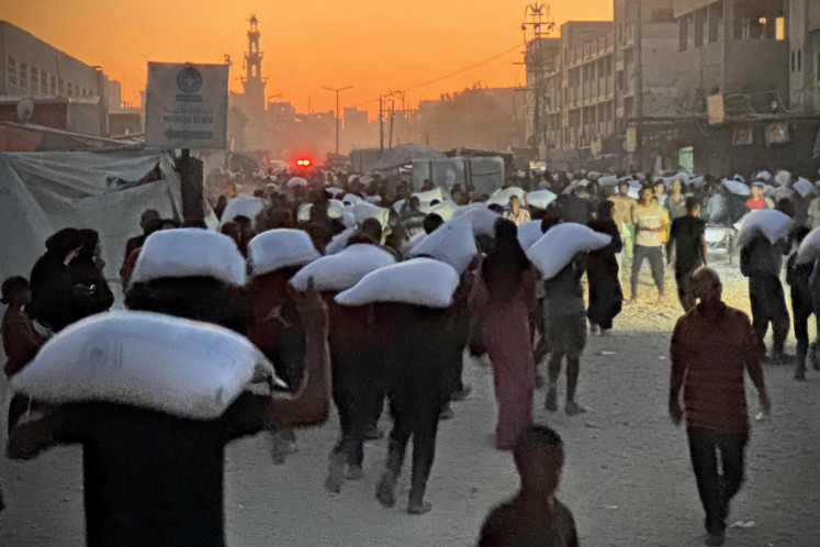 Men walk carrying sacks of flour that were taken from a raided truck carrying foodstuffs, in Khan Yunis in the southern Gaza Strip on July 22, 2025.