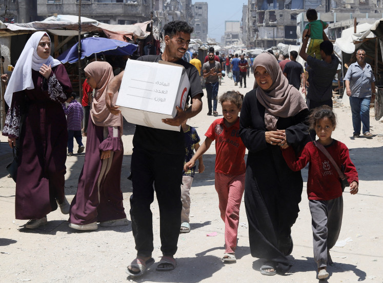 The son of displaced Palestinian woman Iman Suleiman, from Beit Lahiya, carries a box of aid the family received, distributed by the Emirates Red Crescent, in Gaza City, June 26, 2025. 