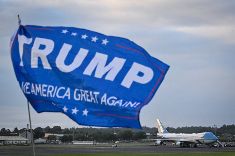 A flag reading “Trump make America Great Again“ flaps on the air as the US president aircraft known as Air Force One lands on the tarmac at Prestwick airport, south of Glasgow on July 25, 2025, on the first day of US President Donald Trump visit in the UK.  Trump departed for Scotland for a mix of diplomacy, business and leisure, as a huge UK security operation swung into place amid planned protests near his family-owned golf resorts.