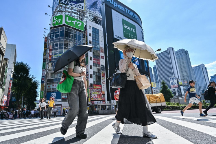 Pedestrians use umbrellas to shelter from the sun as they cross a street in the Kabukicho entertainment area of Shinjuku in central Tokyo, Japan on July 29, 2025.