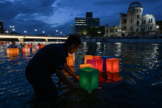 Volunteers push paper lanterns out onto the Motoyasu River past the Atomic Bomb Dome (back right) after they were released by visitors to mark the 80th anniversary of the world's first atomic bomb attack, in the city of Hiroshima on August 6, 2025. 