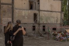 Women stand next to flowers, children's toys, and portraits placed in memory of victims at the site of a nine-story residential building destroyed following a recent Russian missile strike in Kyiv, on August 5, 2025, amid the Russian invasion of Ukraine.