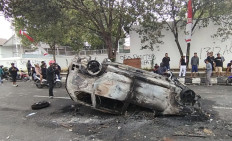 Onlookers check out a burnt car in the wake of an angry protest on Aug. 13 calling for the ouster of Pati Regent Sudewo.