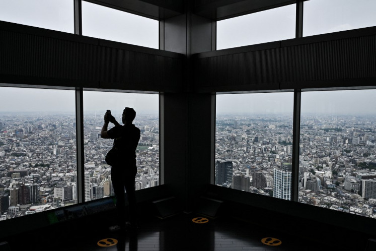 A foreign visitor takes a photo out the windows of the urban sprawl below during a visit to one of the Tokyo Metropolitan Government Building observation decks in the Shinjuku district of central Tokyo on May 16, 2025.