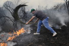 A man uses a branch to fight a wildfire in the village of Veiga das Meas, in Villardevos municipality, northwestern Spain on August 16, 2025. Spain, now in its third week under a heatwave alert, is still battling wildfires raging in the northwest and west of the country, where the army has been deployed to help contain the blazes. The regions of Castilla y Leon, Galicia, Asturias and Extremadura remain the hardest hit.