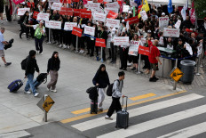 Passengers walk in front of demonstrators holding placards as Air Canada flight attendants said they will remain on strike and challenge a return-to-work order they called unconstitutional, defying a government decision to force them back to their duties, at Vancouver International Airport in Richmond, British Columbia, Canada, on Aug. 17, 2025.