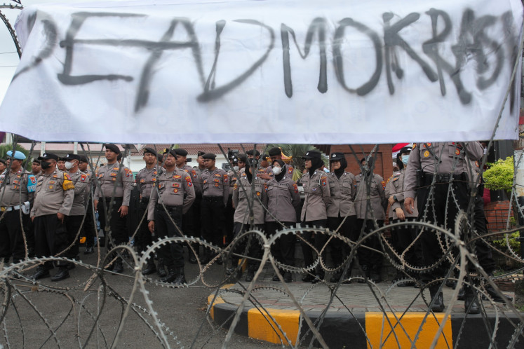 Police officers stand guard behind a razor wire barrier at the East Java Legislative Council (DPRD) in the provincial capital Surabaya on Aug. 19, 2025, during a student-led rally to push for protection of free speech and demand that the government scrap its controversial national history textbook project.