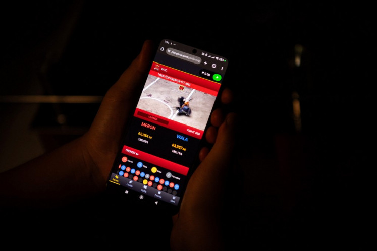 In this photo taken on July 15, 2025, Jay, a graphic artist, watches a live cockfight on his mobile phone in Bulacan province, north of Manila. The 24-year-old, who asked to use a pseudonym as he fears his family's judgment, took just seconds to pull up a live cockfight on his phone for AFP journalists.