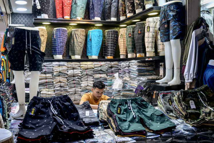 A man uses his phone while waiting for customers at a clothing shop in Tanah Abang Market in Jakarta on March 6, 2025. Buying new clothes is a common tradition among Muslims to celebrate Idul Fitri, which marks the end of the holy month of Ramadan. 