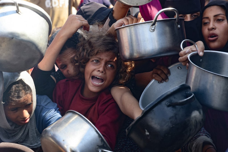 Palestinian women and children hold out their empty pots in front of a charity kitchen in Khan Yunis in the southern Gaza Strip on August 21, 2025. Rights group Amnesty International earlier this week accused Israel of enacting a “deliberate policy“ of starvation in Gaza. Israel heavily restricts aid coming into Gaza but has repeatedly rejected claims of deliberate starvation.