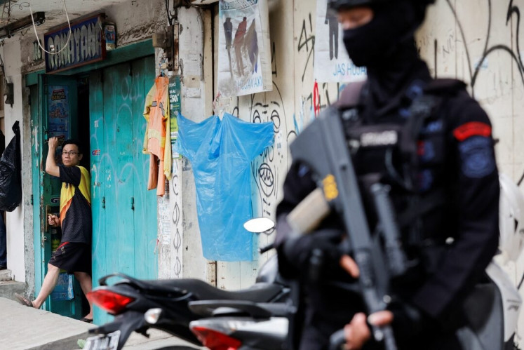 Sense of security: A man looks out from a shop as an armed police officer stands guard following a blast at a district police station, which suspectedly was a suicide bombing, in Bandung, on Dec. 7, 2022. 