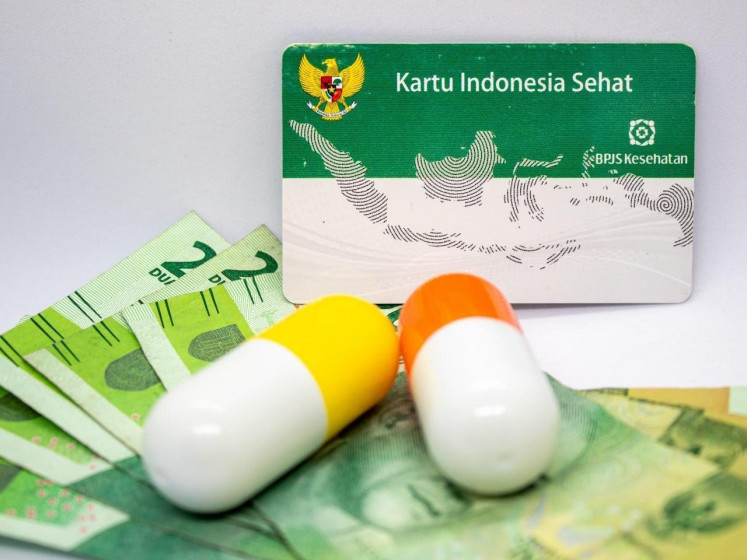 An illustration of the Indonesia Health Card, with medication and rupiah banknotes in the foreground (Courtesy of BPJS Kesehatan)