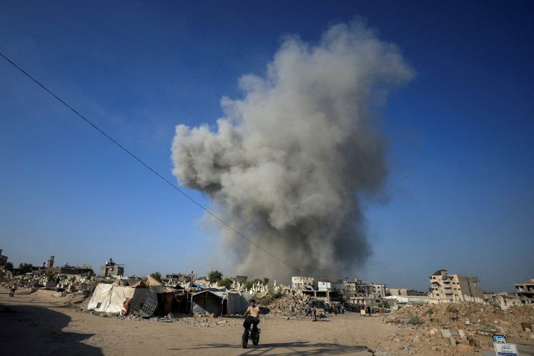  A Palestinian man rides a bike as smoke rises following an Israeli strike, in Gaza City on August 24, 2025.