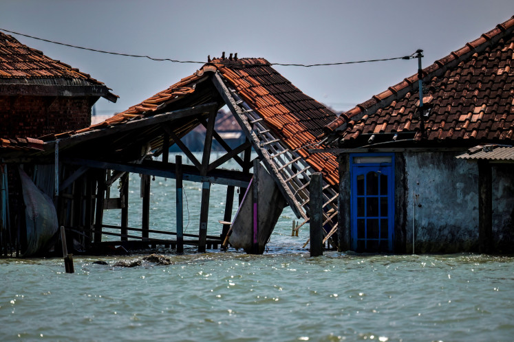 A collapsed house, only its frame and roof tiles remaining, leans in a row of abandoned, partially submerged houses on July 30, 2025, in Bedono village, Demak regency, Central Java, where climate change has contributed to a massive loss of coastal land.
