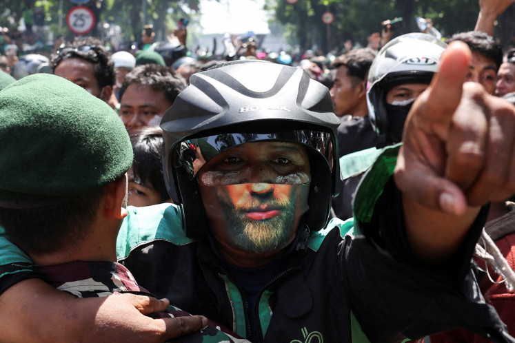 A demonstrator gestures at riot police outside Jakarta Mobile Brigade (Brimob) headquarters in Kwitang, Central Jakarta, during a clash after a motorcycle taxi driver died after being struck and run over by a police tactical vehicle during Thursday's protest on a number of issues including parliamentarians' allowances, education funding and the government's school meals program, on August 29, 2025. 