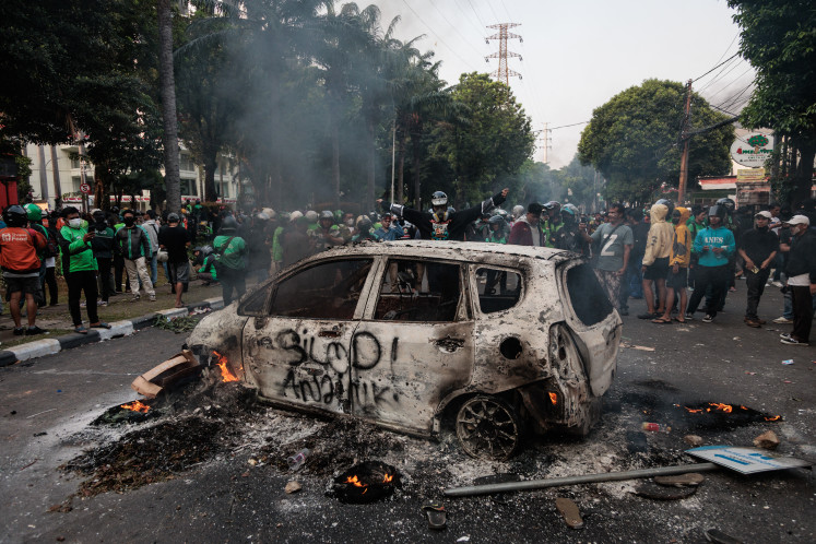 People gather around a burned-out car set ablaze during a protest outside the Jakarta Police’s Mobile Brigade headquarters (Mako Brimob) on Aug. 29, 2025, a day after a motorcycle taxi driver was killed when he was run over by a police tactical vehicle.