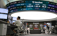 Currency dealers monitor exchange rates beneath a big screen showing South Korea's benchmark stock index (KOSPI) and the Korean won/USD exchange rate in a foreign exchange dealing room at the Hana Bank headquarters in Seoul on June 20, 2025.