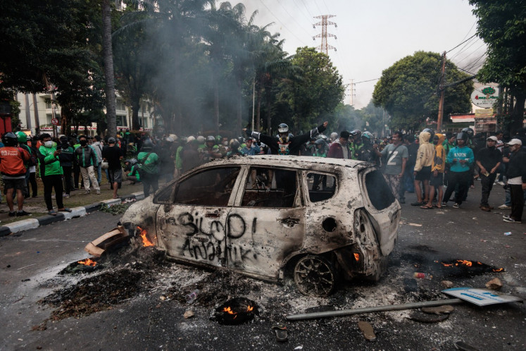 A crowd of protesters surround the burnt frame of a car outside the Central Jakarta headquarters of the Jakarta Metropolitan Police’s Mobile Brigade (Brimob) on Aug. 29, 2025, the day after a Brimob tactical vehicle ran over and killed on-demand motorcycle driver Affan Kurniawan, 21, as he was trying to flee the area of a labor protest that had turned violent