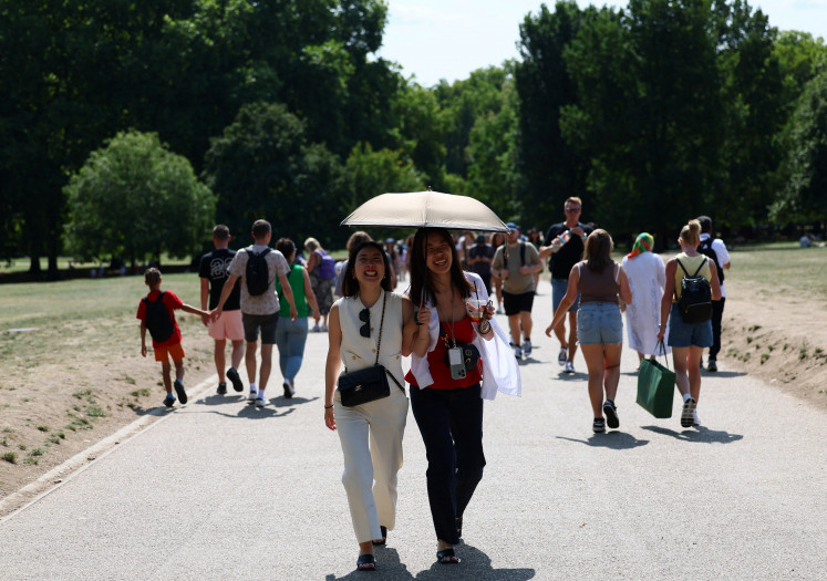 Women shelter from the sun under an umbrella at Green Park during a hot and sunny day, in London, Britain, August 15, 2025.