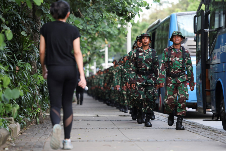 A woman in fitness gear walks toward a line of uniformed members of the Indonesian Military (TN) on Sept. 2, 2025, outside National Monument Park in Gambir, Central Jakarta.