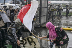 A woman in a pink hijab strikes a police officer with a bamboo pole bearing the national flag during a protest on Aug. 28, 2025, as riot police try to repel a crowd of demonstrators outside the Senayan legislative complex in Jakarta.